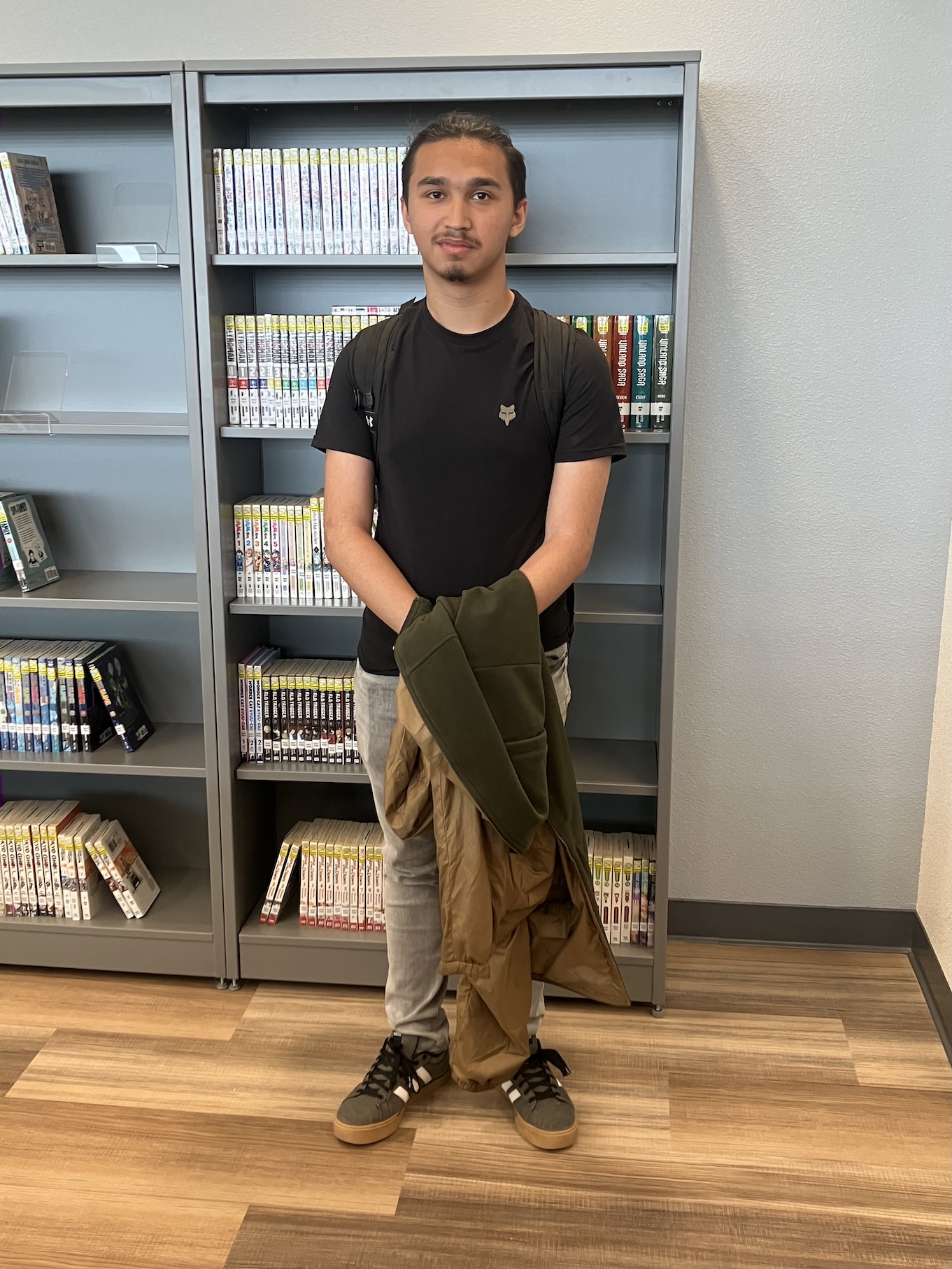 Roberto, winner of the spelling bee, stands in front of a metal bookcase.